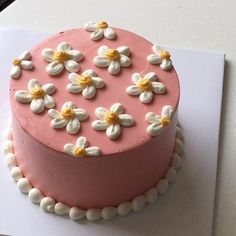 a pink cake with white and yellow flowers on it sitting on top of a piece of paper