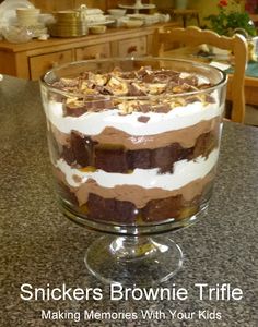 there is a dessert in the glass bowl on the kitchen counter with words that read, snickkers brownie trifle making memories with your kids