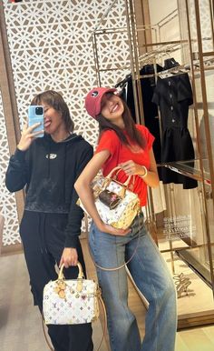 two people standing in front of a store display holding purses and taking pictures with their cell phones