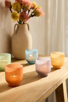 four glass cups sitting on top of a wooden table next to a vase with flowers in it