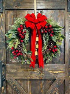 a christmas wreath with holly, pine cones and red ribbon hanging on a wooden door