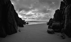 a black and white photo of a person sitting on the beach in front of some rocks