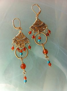 Earrings in an ethnic bohemian style composed of engraved gold-plated fans and twisted rings, Carnelians and Turquoises. Two measuring fans and two closed twisted rings measuring 17 mm in diameter. Cornalines of 6 mm and 3 mm, small Turquoises of 3 mm. Gold plated hooks with lever-back. These earrings measure 8 cm or 3 inches from top to bottom. Bohemian Bronze Earrings With Dangling Beads, Bohemian Bronze Earrings With Intricate Design, Bohemian Bronze Jewelry With Intricate Design, Bohemian Antique Gold Drop Earrings, Bohemian Bronze Jewelry With Dangling Beads, Antique Gold Bohemian Jewelry, Bohemian Gold Jewelry With Intricate Design, Gold Carnelian Dangle Earrings, Bohemian Antique Gold Copper Earrings