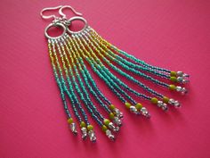 a pair of earrings with beads hanging from them on a pink tablecloth, next to some scissors