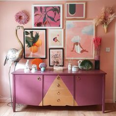 a pink dresser topped with lots of art next to a wall covered in pictures and flowers