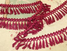 two pieces of red crocheted fabric with tassels on top of it