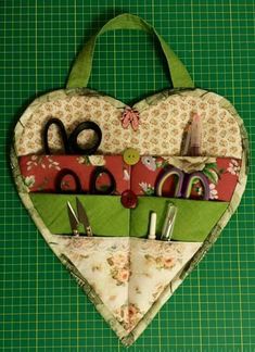 a heart shaped bag with scissors and sewing supplies inside it on a green cutting mat