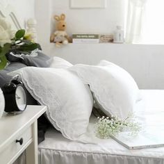 a bed with white sheets and pillows on top of it next to a vase filled with flowers