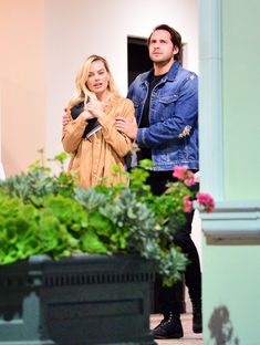 a man and woman standing next to each other in front of potted planters