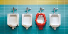 four urinals are lined up in a row on a blue tiled bathroom wall