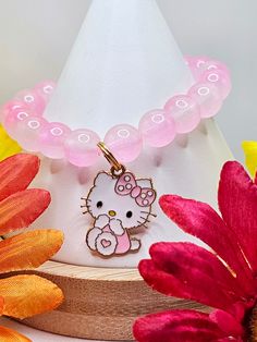 a pink hello kitty necklace sitting on top of a table next to flowers and a white hat