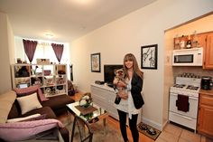 a woman is holding a dog in her living room with the kitchen and dining area behind her