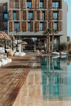 an empty swimming pool in front of a large building with wooden balconies and palm trees