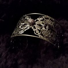 a silver cuff with flowers and vines on it's side, in the dark