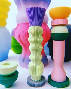 several different colored vases sitting next to each other on top of a white surface