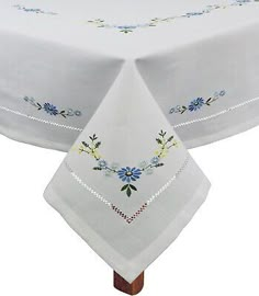 a white table cloth with blue flowers and leaves on the top, sitting on a wooden stand