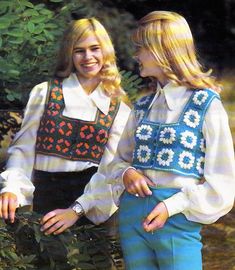 two young women standing next to each other in front of some trees and bushes,