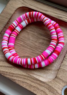 two pink and white bracelets sitting on top of a wooden board