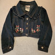 a denim jacket with flowers embroidered on the front and back, sitting on a white surface