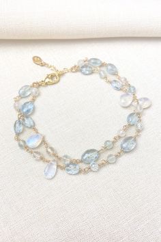 This bracelet showcases delicate moss aquamarine gemstones paired with radiant rainbow moonstones, creating a lovely, feminine style. The artisan meticulously hand-wire-wraps each gemstone bead, creating a beautiful, double-layered chain. The lobster claw clasp and extender chain allow for an adjustable fit. Bracelet length: 7 inches plus 1-inch extender chain Materials: aquamarine, rainbow moonstone, gold fll Dainty Blue Moonstone Jewelry, Elegant Aquamarine Bracelets With Natural Stones, Elegant Hand Wrapped Moonstone Jewelry, Elegant Hand-wrapped Moonstone Jewelry, Elegant Moonstone Gemstone Beaded Bracelets, Moss Aquamarine, Layered Chain, The Lobster, Moonstone Bracelet