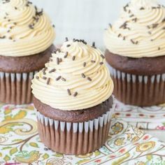 three chocolate cupcakes with frosting and sprinkles on a plate