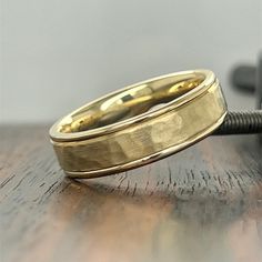 two gold wedding bands sitting on top of a wooden table next to a black phone