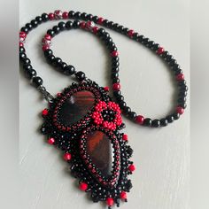 a beaded necklace with red and black beads is displayed on a white table top