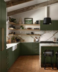 a kitchen with green cabinets and marble counter tops, two bar stools in the center