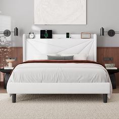 a white bed sitting in a bedroom next to a wall mounted clock and two nightstands