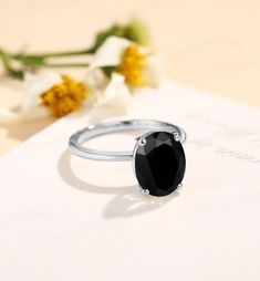 a black diamond ring sitting on top of a piece of paper with flowers in the background