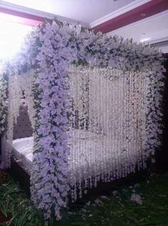 a bed covered in white flowers next to a window with lots of greenery on it