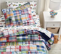 a bed with colorful plaid sheets and pillow cases on top of it next to a night stand