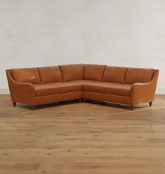 a brown leather sectional sofa sitting on top of a hard wood floored floor next to a white wall