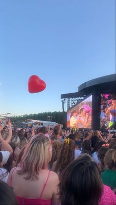 a large group of people at an outdoor concert with a red heart shaped object in the air