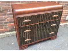 a brown wooden dresser sitting on top of a sidewalk next to a brick wall,