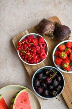 fruits and vegetables are arranged in bowls on a cutting board next to a watermelon