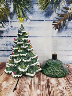 a small christmas tree next to a green bell on a wooden table with snowflakes