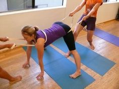 three women are doing yoga on blue mats in an office setting with one woman pulling the other