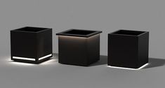 three black square vases sitting next to each other on a gray surface with light coming through them