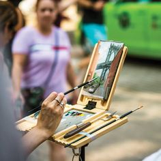 a person is painting on an easel with paintbrushes and watercolors