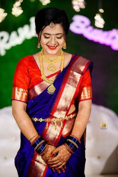 a woman in a blue and red sari with gold jewelry on her neck smiling