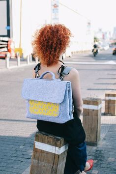 a woman with red hair sitting on top of a wooden bench wearing a blue backpack