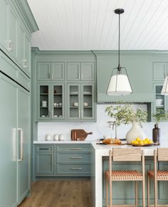 a kitchen with green cabinets and white counter tops, wooden flooring and two stools in front of the island