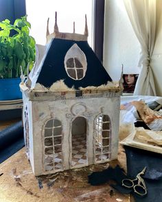 a doll house is sitting on a table next to a potted plant and scissors