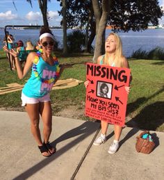 two young women holding signs in front of the water, one with a missing sign on it