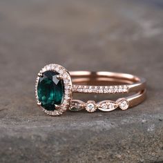 two wedding bands with an oval cut green stone and diamond set in rose gold, on top of a rock