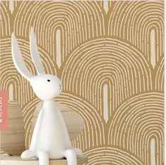 a white rabbit figurine sitting on top of a wooden table next to a wallpaper