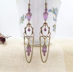 This listing is for my ornate Victorian inspired handmade earrings.  The earrings are made by me with new components but are made to look like fine Vintage treasures!  I have used gorgeous top quality genuine Czech Glass flower beads in a soft purple shade with metallic subtle bronze accents.  I have accented these with high quality Amethyst purple crystal beads.  All additional elements including the stunning intricate chandelier connectors and chains are done in antiqued brass metal. These are Handmade Victorian Chandelier Drop Earrings, Victorian Chandelier, Romantic Academia, Flower Chandelier, Antique Brass Metal, Earrings Purple, Purple Crystal, Soft Purple, Flower Beads