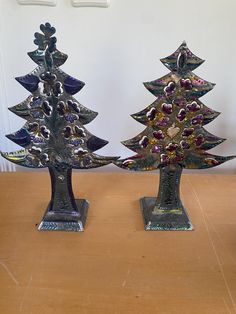 two metal christmas trees sitting on top of a wooden table