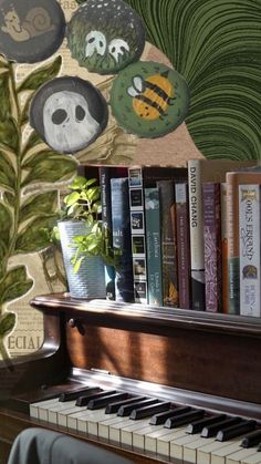 an old piano with books on it in front of a wallpapered background and plants